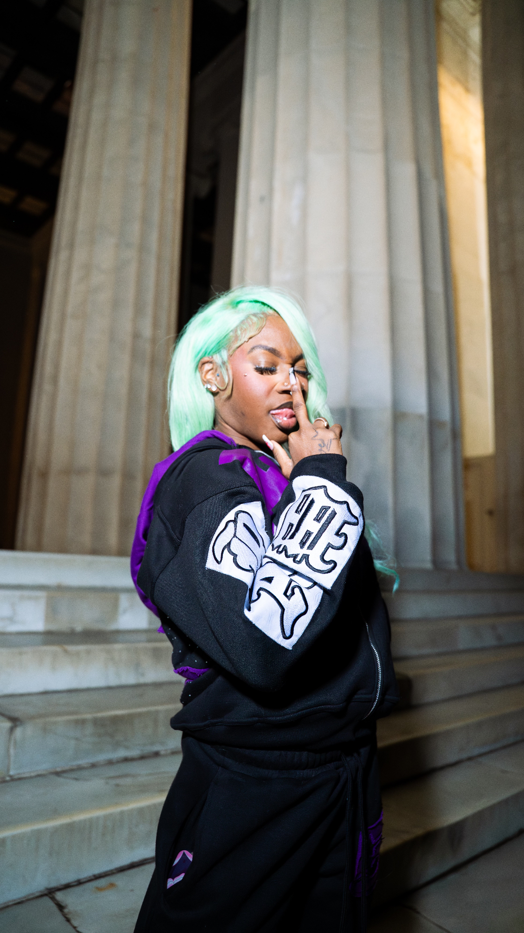 UNFLTRD model with mint green hair wearing a black zip-up with purple hood
